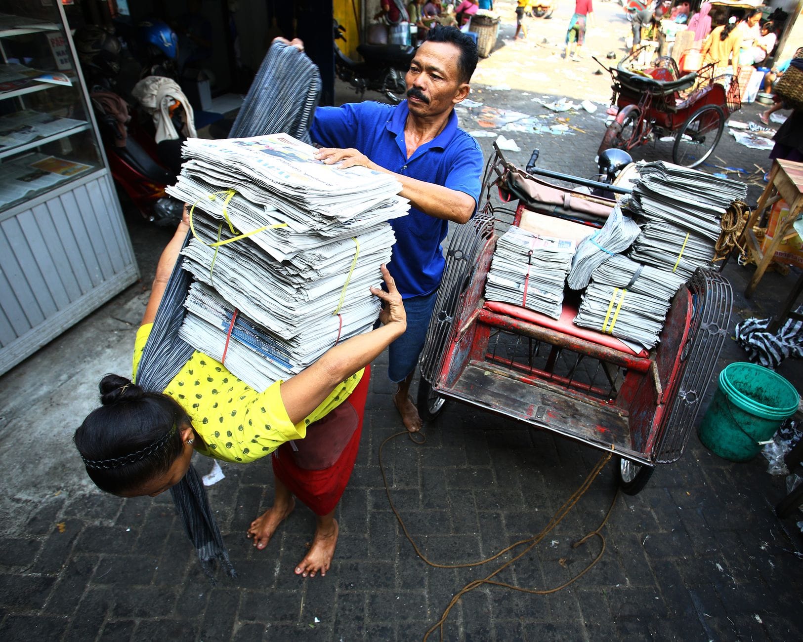 Street vendors transferring newspapers on a busy street in Surakarta, Indonesia, showcasing local hustle.